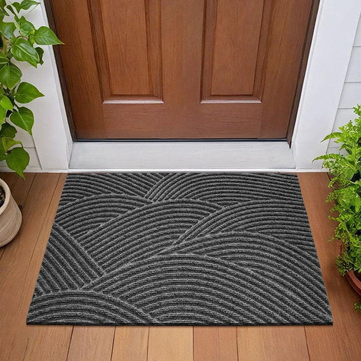 Dark grey 3D wave-patterned doormat placed outside a wooden door with potted plants.