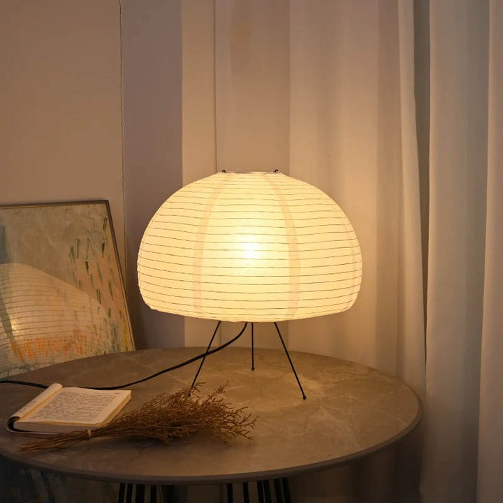 Round white rice paper lantern lamp with black tripod base, soft LED light for Japandi-style interiors.