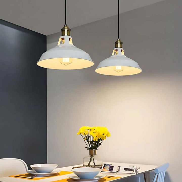 Two white pendant lights hanging above a dining table with a vase of yellow flowers on a gray wall background.