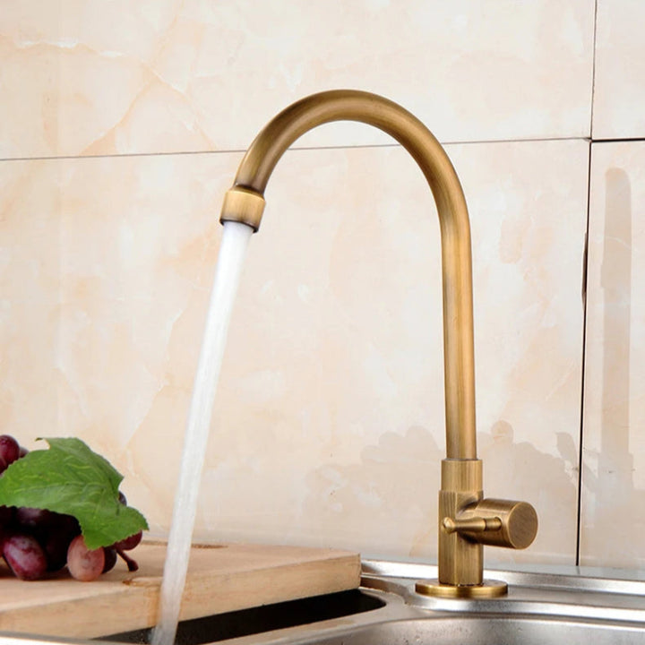 Gold kitchen faucet with water flowing into a sink, with grapes and a cutting board on the counter.