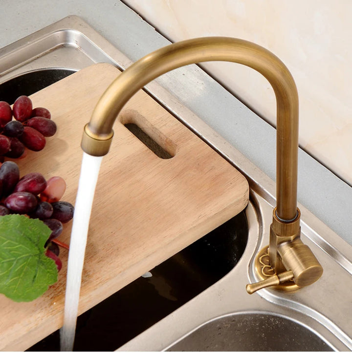Gold kitchen faucet with water flowing into a sink, next to a cutting board with grapes and lettuce.