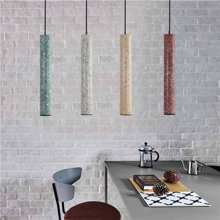 Four cylindrical pendant lights hanging above a dining table with a brick wall background.