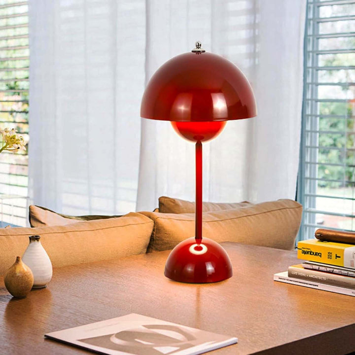 Glossy red retro flower bud table lamp with spherical base and dome shade, illuminating a wooden coffee table in a mid-century style living room.
