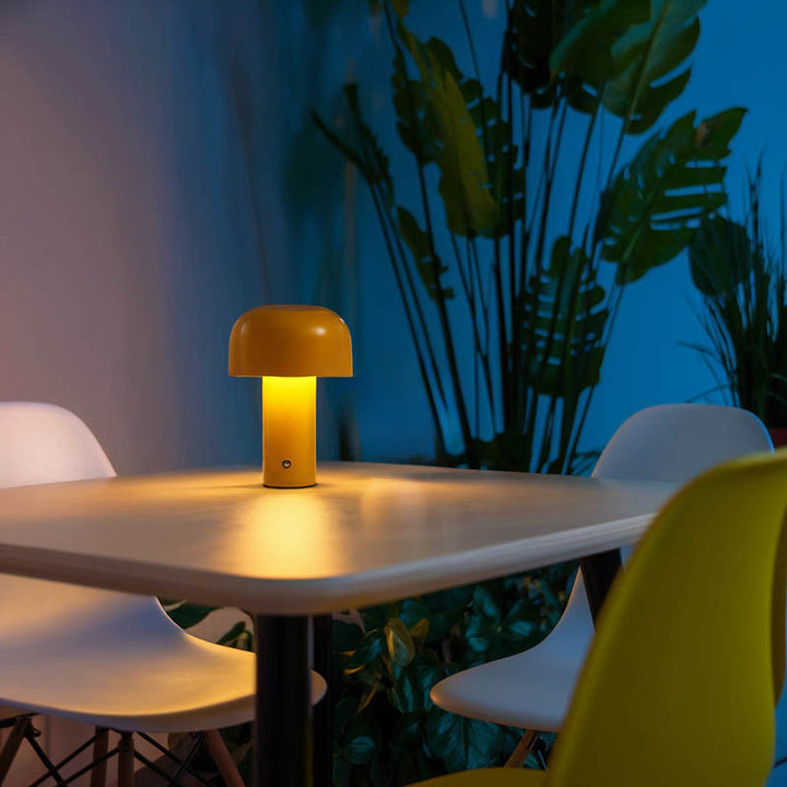 Modern yellow cordless mushroom lamp on dining table, warm LED glow, portable metal design for indoor or outdoor use.