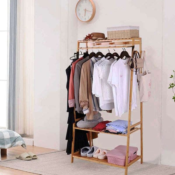 Freestanding bamboo clothes rack with top shelf, hanging rail, and two lower storage shelves, styled in a Nordic bedroom with folded garments.