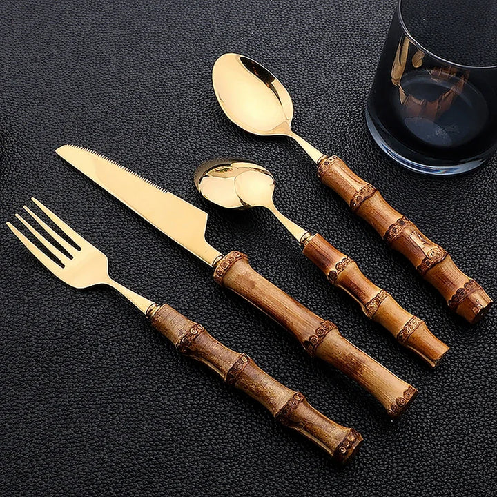 Set of gold cutlery with brown bamboo handles on a black surface