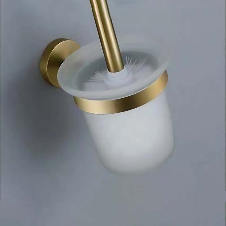 Bathroom brush holder with gold finish and white cup on a light gray background