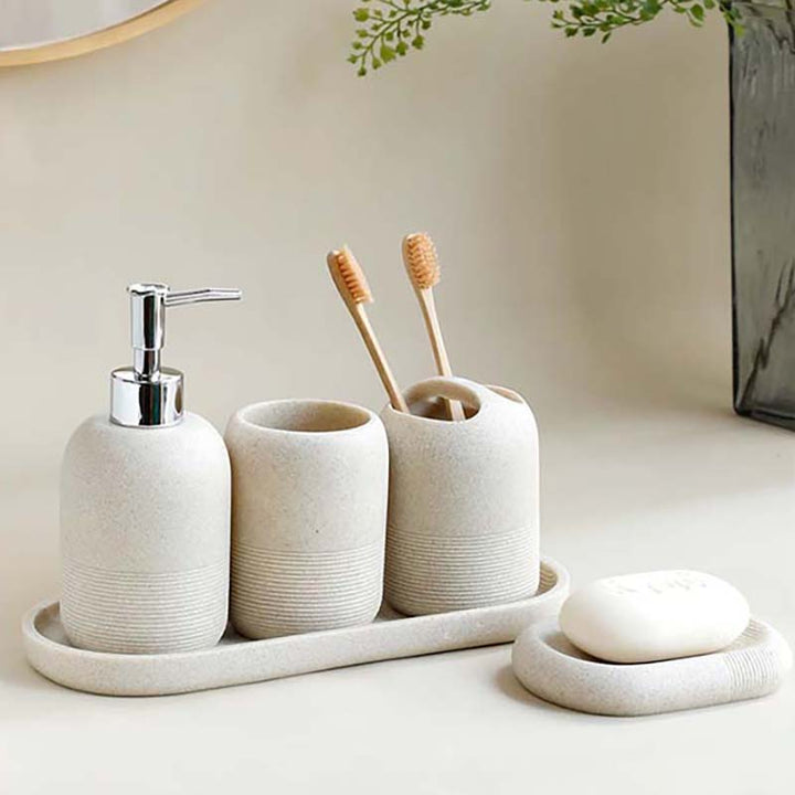 Bathroom set with ceramic items including a soap dispenser, toothbrush holders, and a tray on a neutral background.