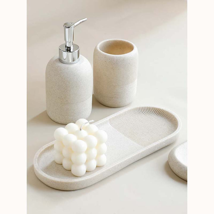 Bathroom accessories set with a soap dispenser, toothbrush holder, and tray on a light surface.