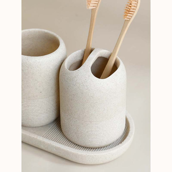 Two stone-colored ceramic toothbrush holders with bamboo toothbrushes on a matching tray.
