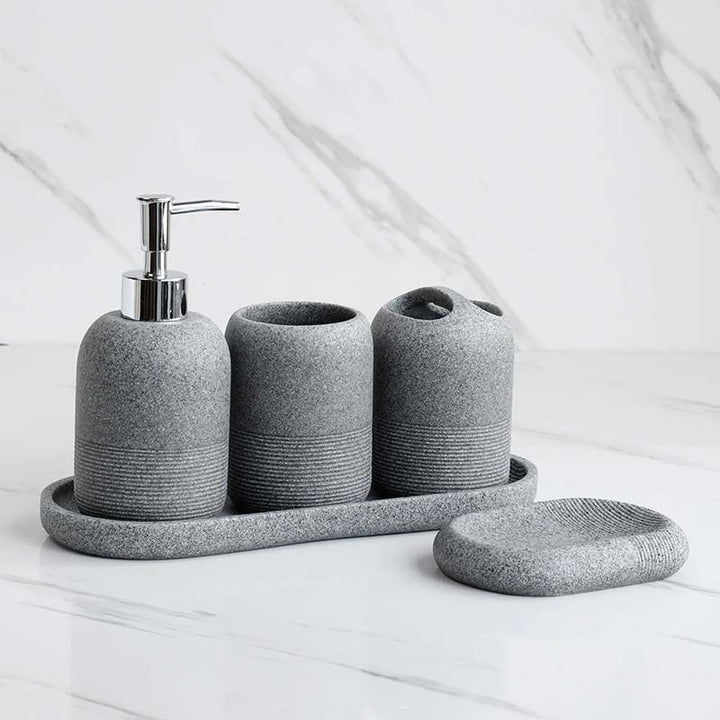 Gray textured bathroom accessory set including a soap dispenser, toothbrush holder, and tray on a white surface.