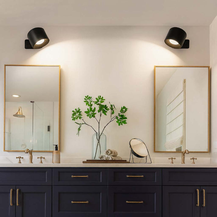 Bathroom vanity with two mirrors, black fixtures, and a vase with greenery.