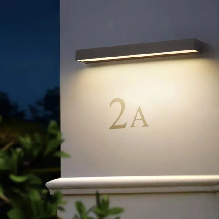 Modern black outdoor wall light illuminating house number, sleek aluminum fixture.
