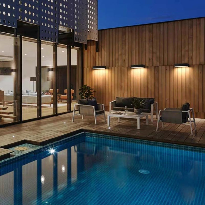 Three black aluminum outdoor wall lights illuminating a modern patio with pool at dusk.