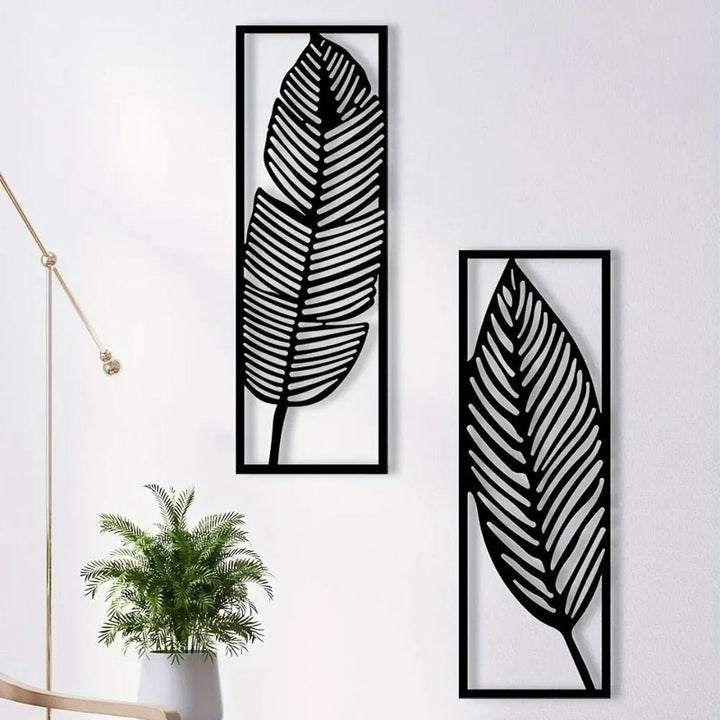 Two black leaf-shaped wall art pieces on a white wall with a plant below.