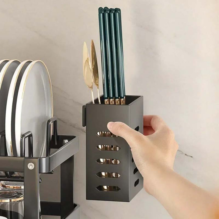 Hand holding a black knife block with green knives next to a dish rack.