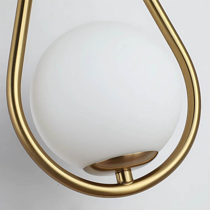 ​Close-up of drop-shaped brass wall lamp with frosted glass diffuser.
