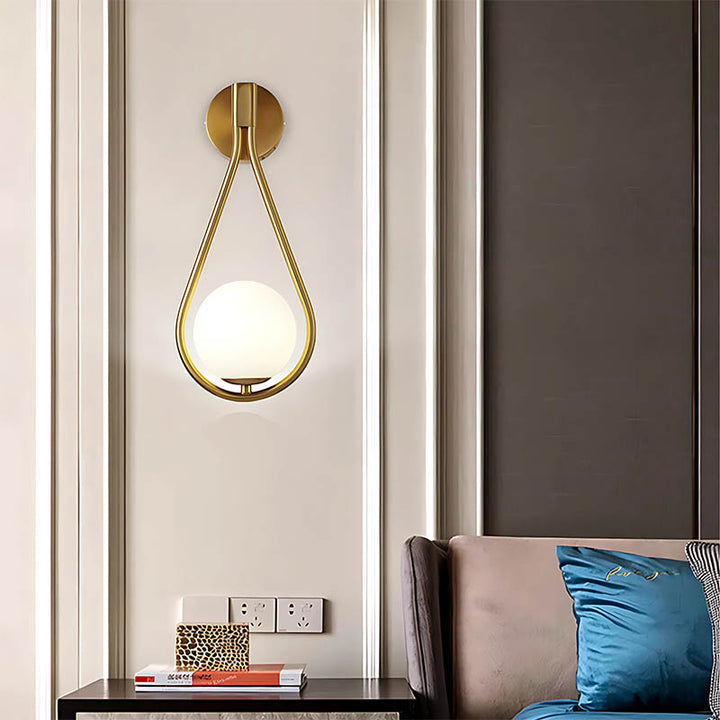 Brushed brass wall light with frosted glass globe illuminating modern bedrom.