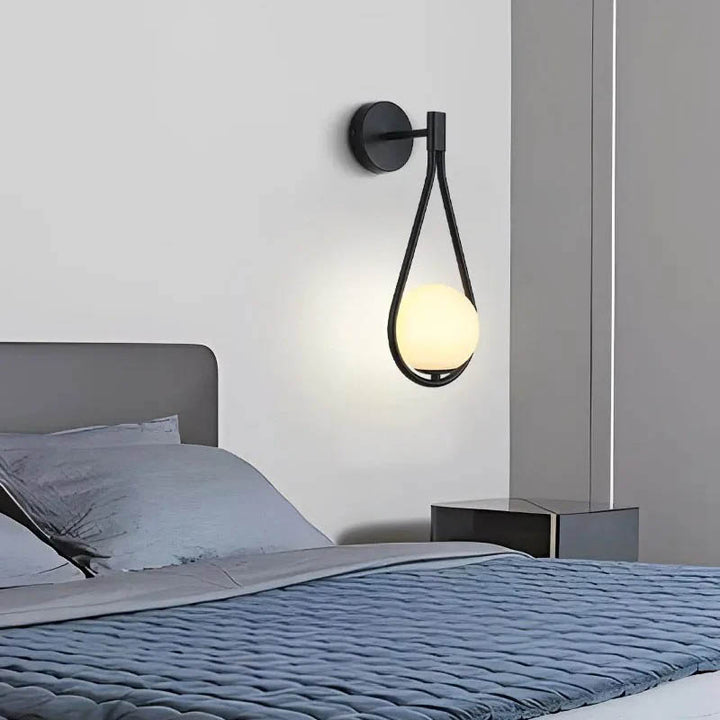 Satin black Nordic wall sconce beside bed, casting soft ambient light in a modern bedroom interior.