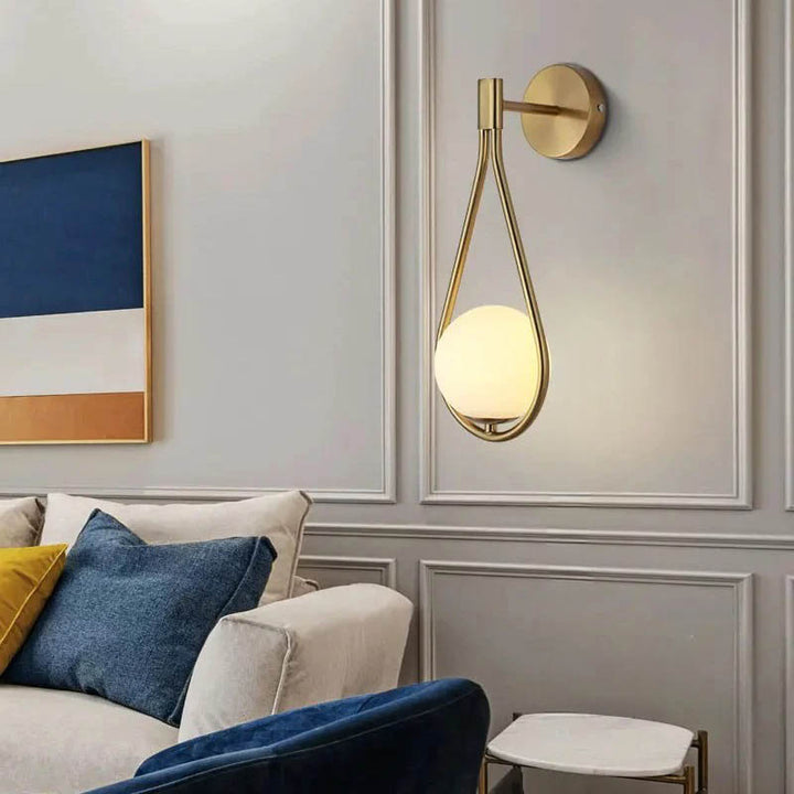 Brushed brass wall light with frosted glass globe illuminating modern living room.
