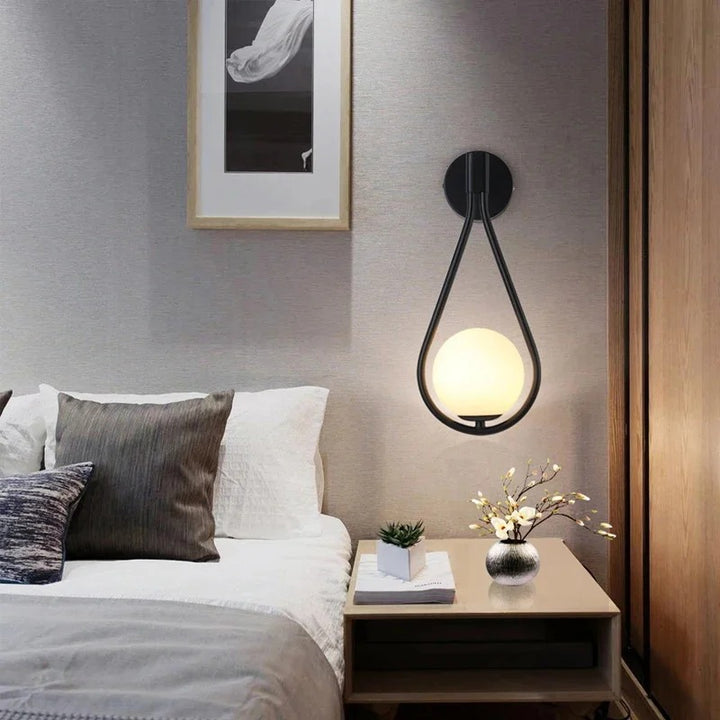 Satin black Nordic wall sconce beside bed, casting soft ambient light.