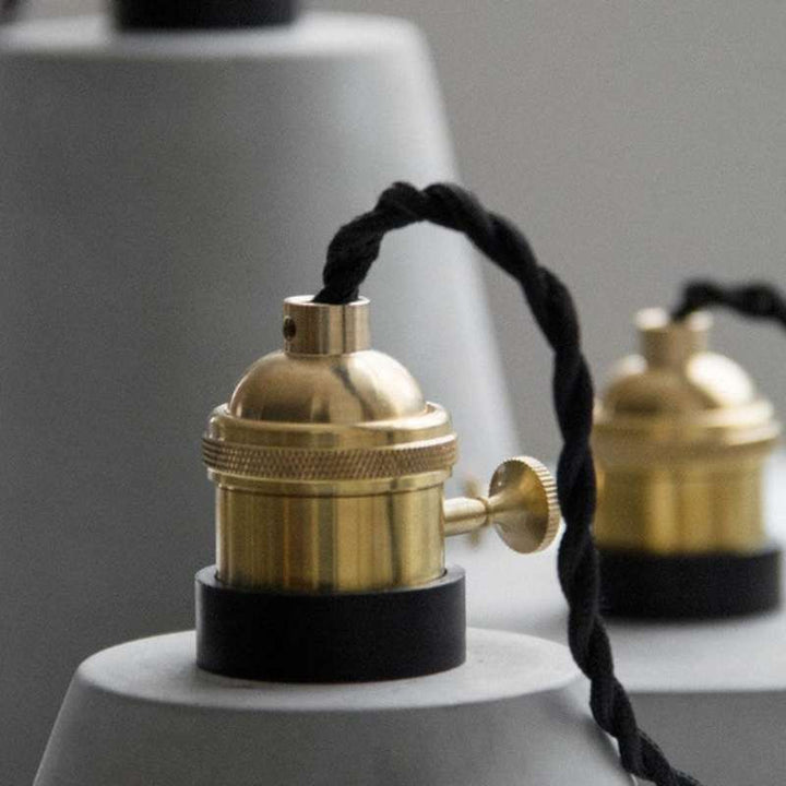 Close-up of brass lamp socket with black braided cord on grey concrete pendant base