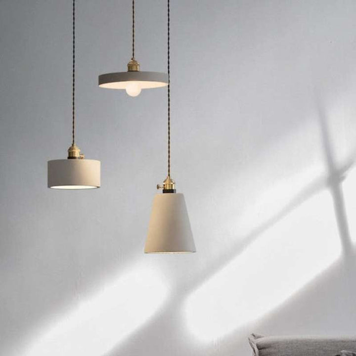 Trio of Nordic concrete pendant lights with brass fittings casting warm light on wall