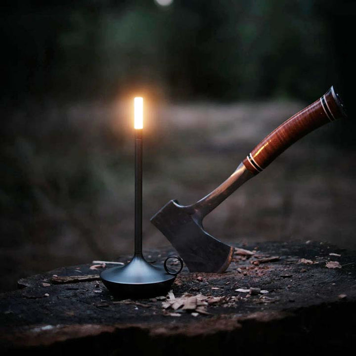 Matte black ALLADIN touch LED lamp glowing on a tree stump beside an axe – ideal for portable outdoor UK ambient lighting.