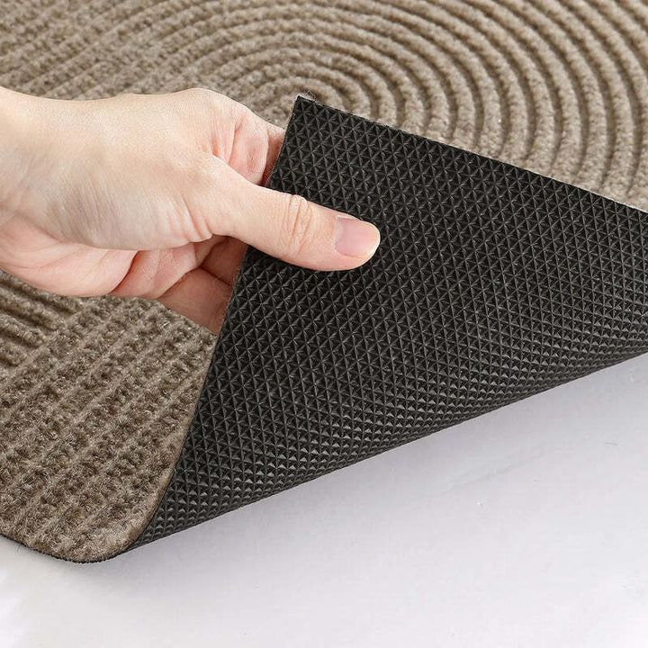 Close-up of hand lifting beige doormat to reveal textured black TPR non-slip backing for secure grip.