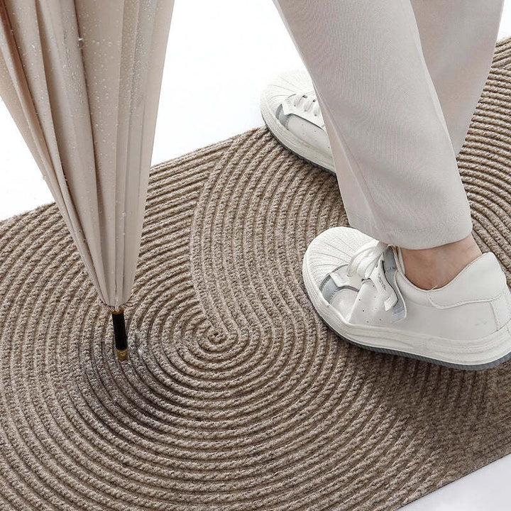Person stepping on beige circular-patterned doormat with umbrella, showing its water-absorbent design.