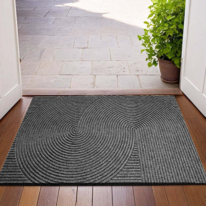 Dark grey circular-patterned 3D doormat at entrance, contrasting beautifully with wooden floor and plants.