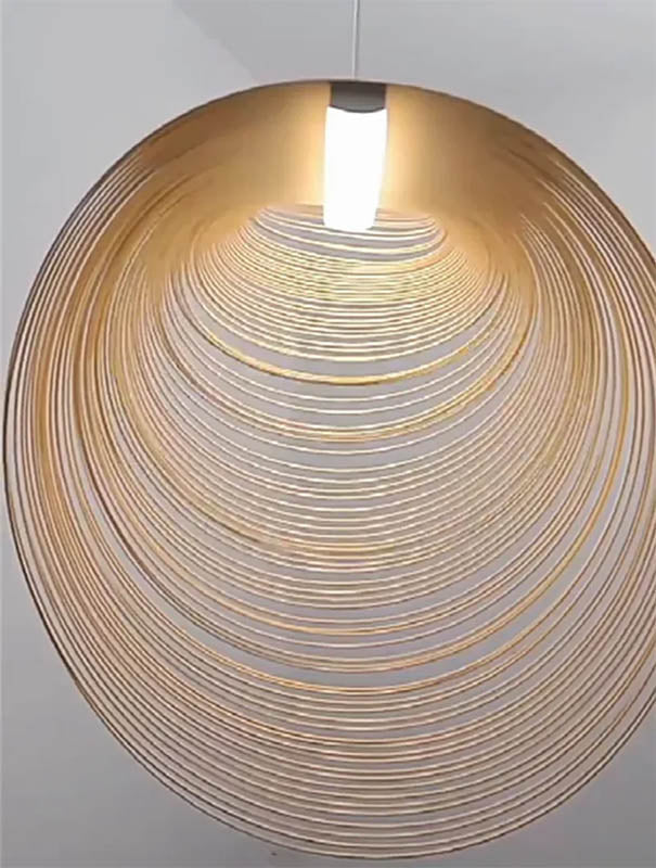 Minimalist beech wood pendant lamp viewed from side, suspended on white background to show sculptural curve.