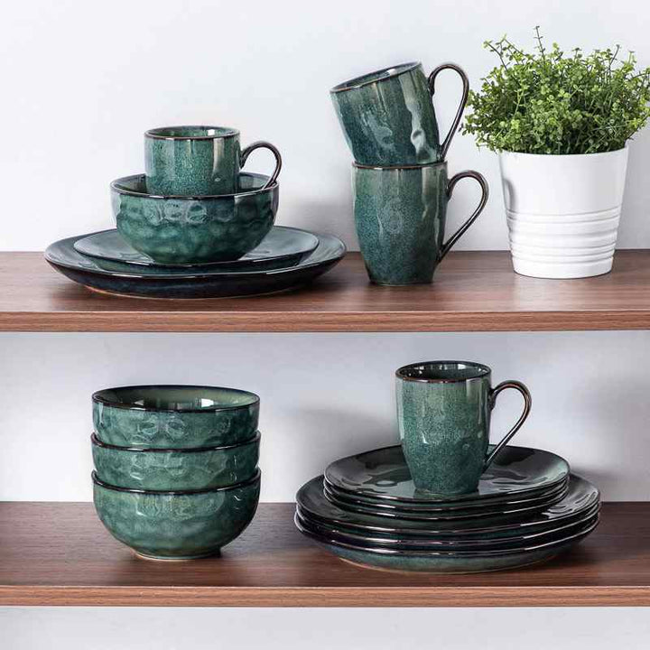 Teal ceramic dinnerware  set on wooden shelves with a plant in the background.