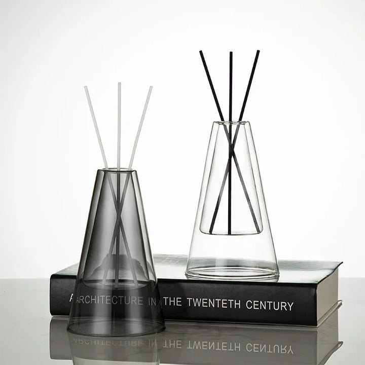 Transparent and smoky grey glass diffusers with reed sticks displayed on stacked books