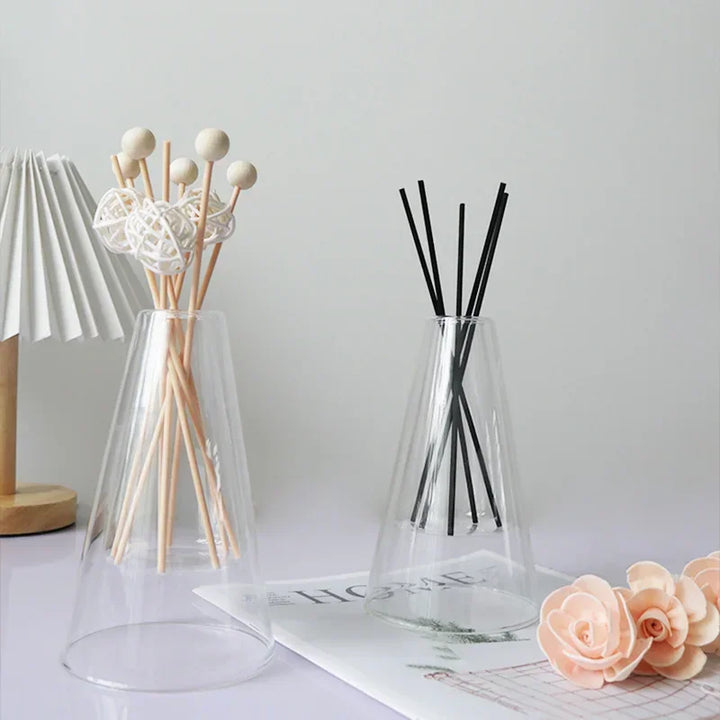 Glass diffuser with reed sticks styled on desk beside lamp and decorative flowers for home décor