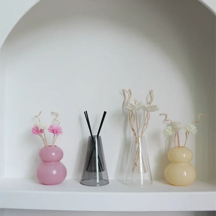 Transparent glass essential oil diffusers and decorative vases with floral arrangements on a white shelf.