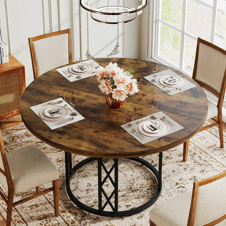 Round wooden dining table with chairs and place settings in a bright room.