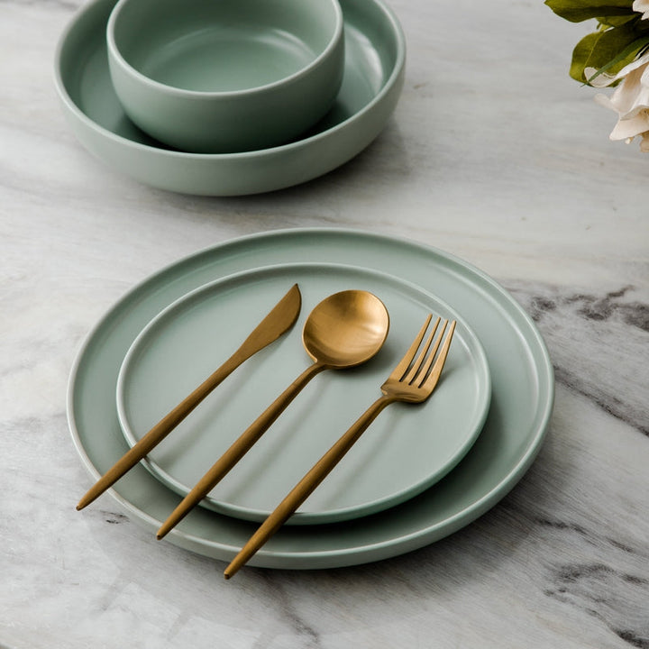 Green ceramic plates with gold cutlery on a marble surface