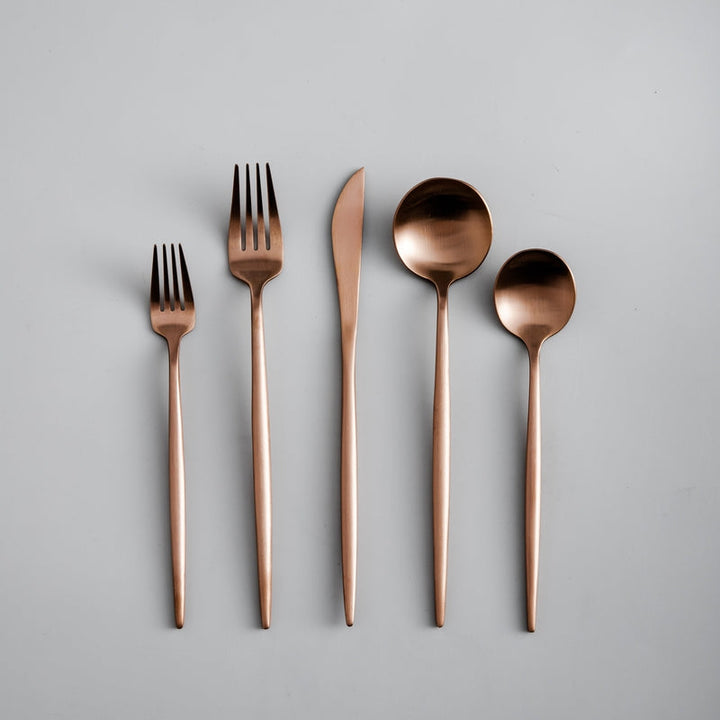 Set of rose gold cutlery including forks and spoons on a gray background
