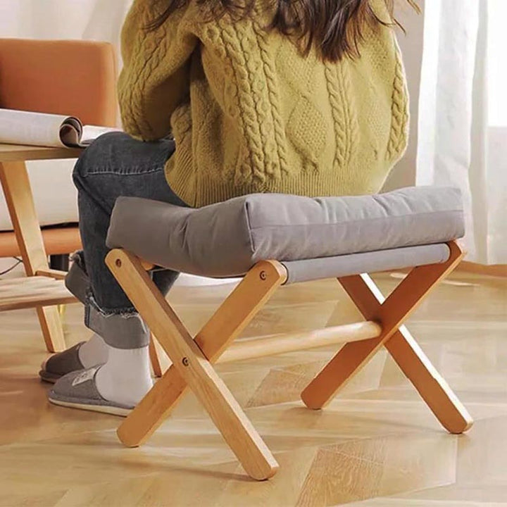 Compact wooden stool with thick grey cushion, used as a seating bench, combining minimalist design with functional comfort.