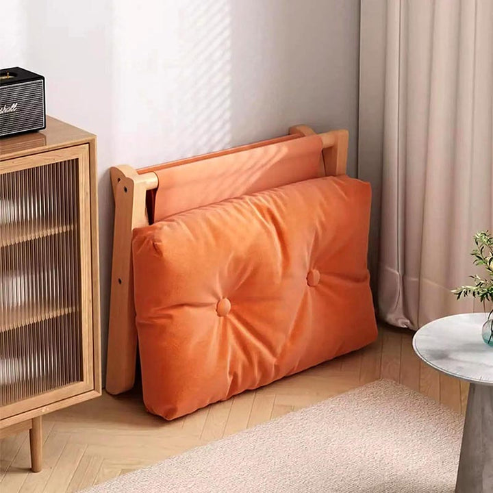 Folded wooden ottoman with thick orange cushion leaning against wall, showing space-saving design for modern minimalist UK homes.