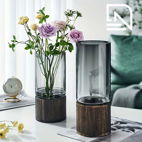 Two cylindrical vases with wooden bases on a table, one containing flowers.