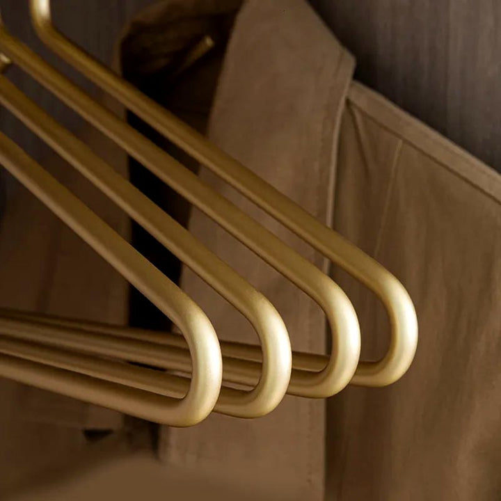 Close-up of three matte gold aluminium hangers, smooth finish and rounded edges for premium closet organisation.