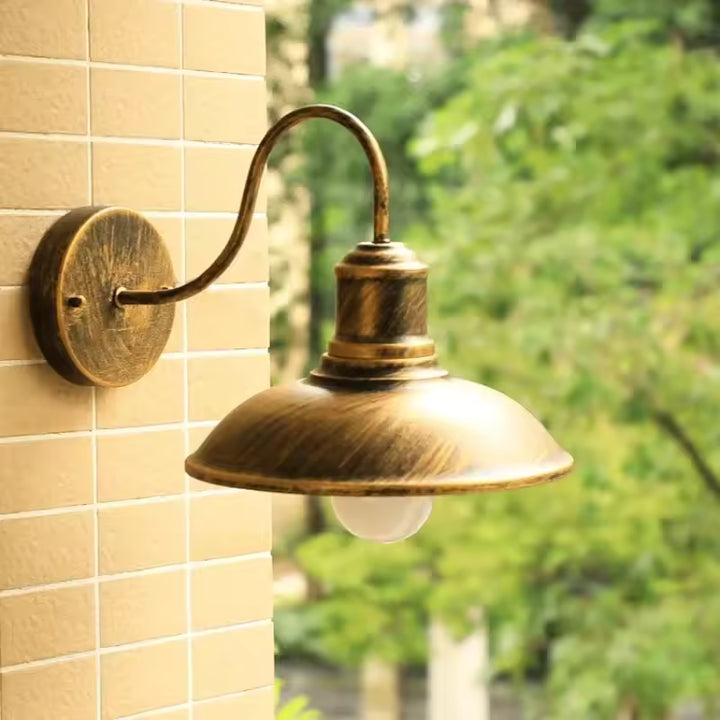 Bronze retro industrial outdoor wall lamp with brushed finish, curved arm and LED bulb, fixed on tiled exterior wall