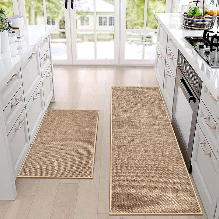 Two woven kitchen rugs on a kitchen floor with white cabinets and appliances in the background.