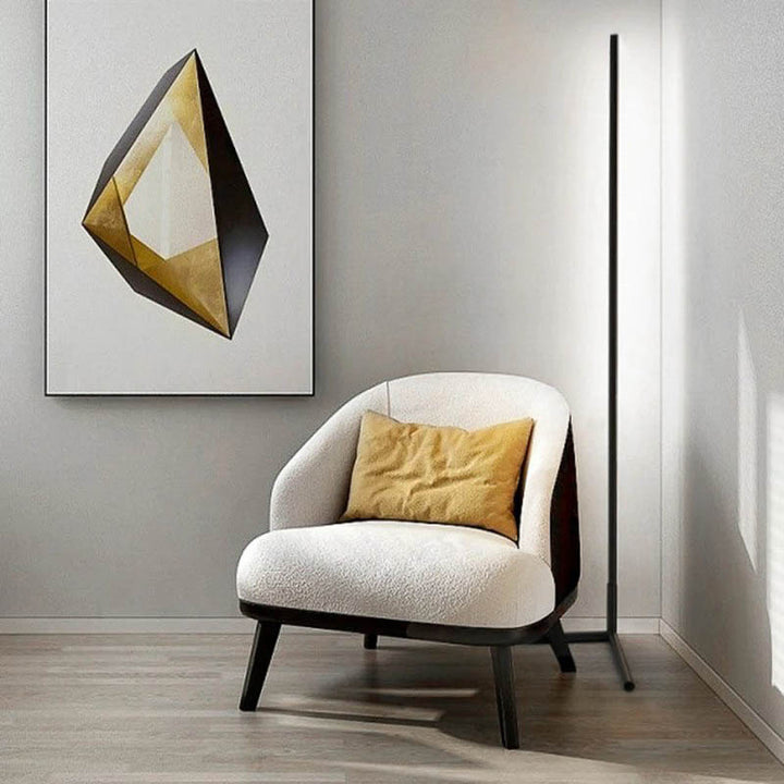 Modern armchair with a yellow pillow in a room with a geometric wall art piece and led floor lamp.
