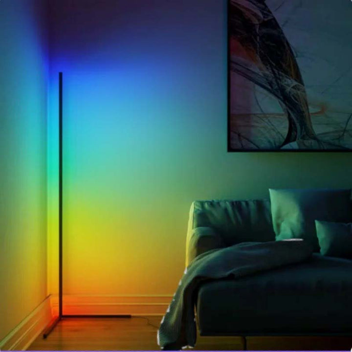 Bedroom with a floor lamp casting  a colorful gradient light on the wall and a bed with pillows.