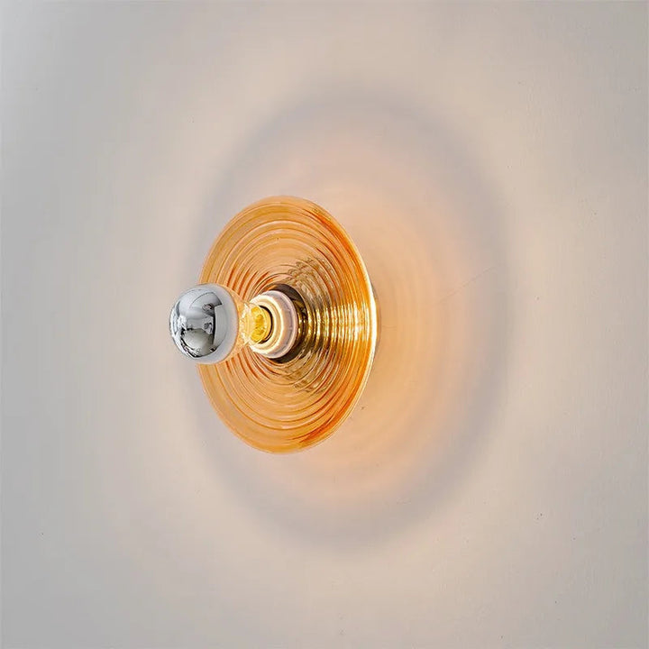 Wall-mounted light fixture with gold and silver design on a neutral background