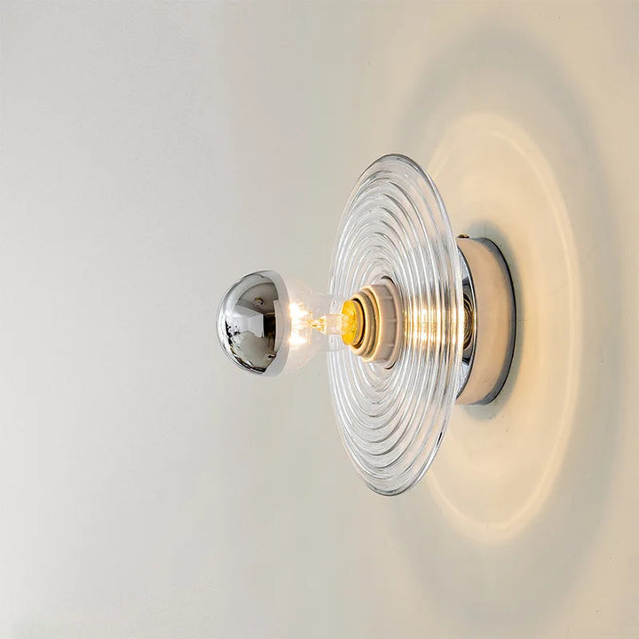 Wall-mounted light fixture with clear glass shade on a white wall