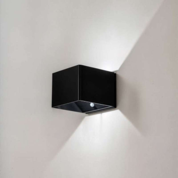 Mounted black LUMA LED wall lamp with warm light beam, motion sensor activated for hallway or living room
